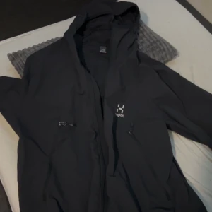 Svart jacka från Haglöfs - Säljer en svart jacka från Haglöfs i bra skick. Den har en dragkedja framtill och är perfekt för utomhusaktiviteter. Jackan har en huva och flera praktiska fickor med dragkedjor. Perfekt för höst och vår! Passar Stolek S/M värde av 2799