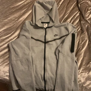 Grå hoodie från Nike - Säljer en grå hoodie från Nike i storlek L. Den har en dragkedja framtill och en praktisk ficka på ärmen. Perfekt för höst och vår, eller när du bara vill chilla. Superbekväm och stilren design!