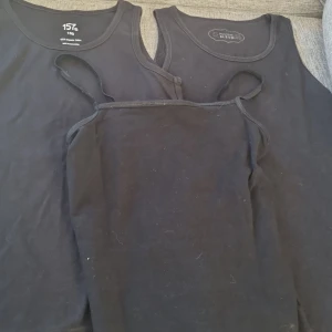Svarta linnen i olika stilar - Säljer tre svarta linnen i olika stilar. Två av dem är klassiska tanktops med breda axelband, perfekt för vardagsbruk. Det tredje är ett mer elegant linne med smala axelband, idealiskt för sommardagar. Alla är i bra skick och gjorda av bekväm bomull. Perfekt basplagg för garderoben! Det är lite smutsigt på lager 157 linnet som man kan tvätta bort!