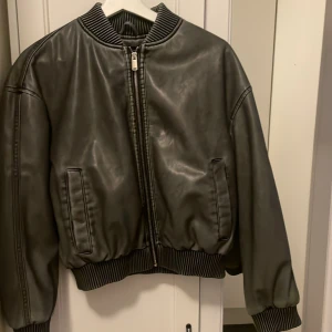 Grå tvättad bomberjacka från Zara - Säljer en snygg svart/grå bomberjacka från Zara i mycket bra skick. Jackan har en dragkedja framtill och ribbade muddar vid krage, ärmslut och nederkant. Perfekt för höst och vår, och ger en cool look till vilken outfit som helst.