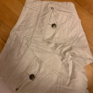 Vita byxor med fina detaljer  - Säljer ett par vita byxor i bra skick. De har flera snygga knappar och en dragkedja framtill. Byxorna är straight leged. Köpt för 250kr säljer för 190kr. Säljer pga av att de inte passar mig i längden för referens är jag 154cm. Byxorna är storlek 36