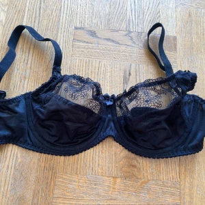 Svart spets-bh - Säljer en elegant svart bh med spetsdetaljer och en söt liten rosett framtill. Den är gjord av 59% polyester och 41% polyamid, vilket gör den både bekväm och hållbar. Perfekt för speciella tillfällen eller när du bara vill känna dig extra fin.