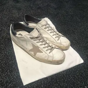 Säljer ett par Golden Goose sneakers i vitt med en ikonisk stjärndetalj på sidan. Skorna har en vintage look med smutsiga detaljer och svart häl. Perfekta för en avslappnad stil. Kommer med originalpåse.