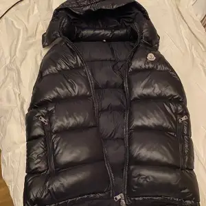 Säljer en snygg svart dunväst från Moncler i mycket bra skick. Västen har en quiltad design med dragkedja och avtagbar huva. Perfekt för höst och vår när du vill hålla dig varm men ändå se stilren ut. Den har också praktiska fickor med dragkedjor. Passar perfekt för en casual look eller när du vill klä upp dig lite extra. 