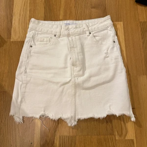 Vit jeanskjol med rå kant - Säljer en snygg vit jeanskjol från Bershka med rå kant och slitna detaljer. Kjolen har en klassisk femficksdesign och är perfekt för sommardagar. Den är i bra skick och passar till både vardag och fest. Superfin att matcha med en färgglad topp eller en enkel t-shirt!