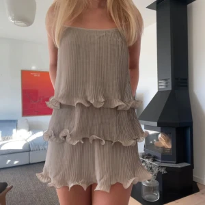 Beige plisserad klänning med volanger - Säljer en superfin beige klänning med plisserat tyg och volanger i flera lager. perfekt för en festlig kväll. Klänningen är i kantarell still 