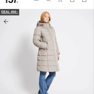 Beige lång dunjacka - Säljer en snygg beige lång dunjacka med huva. Perfekt för kalla dagar, den är både varm och stilren. Jackan har långa ärmar och en quiltad design som ger extra värme. Passar perfekt till vintern och hösten. Ett riktigt kap för den stilmedvetna! Helt ny pris lappen finns kvar 