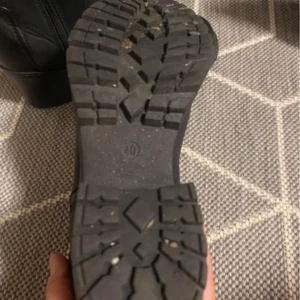 Svarta boots med dragkedja - Snygga svarta boots i skinn med en robust klack och dragkedja i guld. Perfekta för höst och vinter, dessa boots har en grov sula för extra grepp. Storlek dam 40. De är i mycket bra skick och redo för nya äventyr!