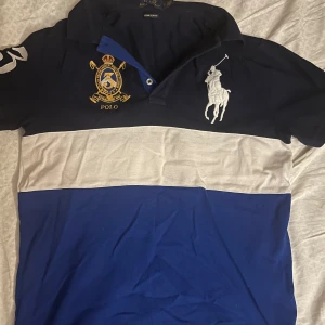 Chief keef type skjorta  - Säljer en snygg pikétröja från Ralph Lauren i blått och vitt. Tröjan har korta ärmar och en klassisk krage. Den är dekorerad med ett stort broderat märke och en polospelare på framsidan. Lite cropped lowkey, kom gärna med prisförslag!🇸🇪🇸🇪🎂🎂