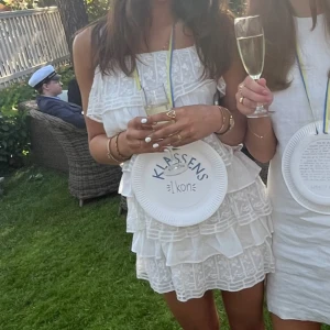 Vit klänning med volanger - Superfin vit klänning med volanger, perfekt för sommarens fester! Den är ärmlös och har en söt, luftig design som passar perfekt till studentfirandet. Klänningen är i ett lätt material som gör den bekväm att bära hela dagen.