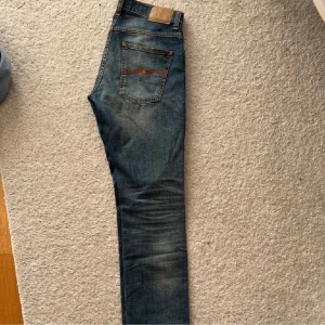 Blå nudie grim tim  - Säljer ett par snygga blå jeans från Nudie i bra skick. Det är nudie grim Tim De har en klassisk femficksdesign med sömmar och en läderpatch med logga baktill. Perfekta för både vardag och fest! 🕺