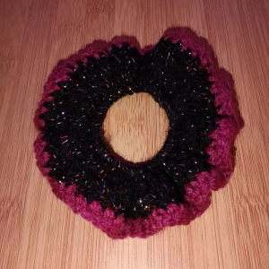 Virkad scrunchie - Snygg och unik virkad scrunchie i svartglitter med lila detaljer. Perfekt för att ge din frisyr en färgglad touch. Den är elastisk och passar de flesta hårtyper. Perfekt accessoarer för både vardag och fest! Skulle du vilja ha en i en specifik färg är det bara att skriva. Alla accessoarer är gjorda av mig.
