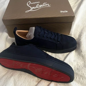 Svarta sneakers från Christian Louboutin - Säljer ett par snygga svarta sneakers från Christian Louboutin i nytt skick. De har den ikoniska röda sulan och är gjorda i skinn. Perfekta för att ge din outfit en lyxig touch. Skorna kommer med originalförpackning och tillbehör.