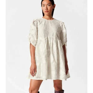 Vit klänning med broderad design - Säljer en superfin vit klänning med broderad design. Den har puffiga trekvartsärmar med knytband och är perfekt till studenten! Endast använd 1 gång och i perfekt skick. Den är i elfenbensfärg. Nypris 1390