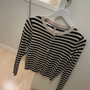 Randig kofta i svart och beige - Säljer en superfin randig kofta i svart och beige. Den har långa ärmar och knappar hela vägen fram. Storleken är normal och materialet känns mjukt och skönt. 