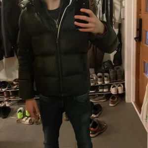 Svart pufferjacka från Tommy Hilfiger - Säljer en svart pufferjacka från Tommy Hilfiger i bra skick. Jackan har en dragkedja framtill och långa ärmar. Perfekt för kalla dagar med sin varma och vadderade design. Den har en liten logga på ärmen som ger en snygg touch. Passar perfekt för höst och vinter!