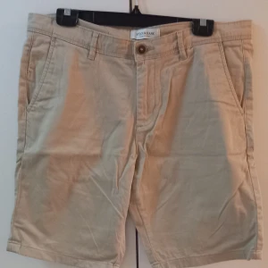 Beige shorts från Dockers - Säljer ett par snygga beige shorts från Dockers i bra skick. De har en klassisk design med knappar och dragkedja framtill. Perfekta för sommaren med en normal passform och tillverkade i ett bekvämt bomullsmaterial. Passar både till vardags och lite finare tillfällen.