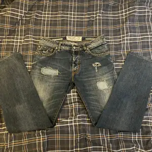 Säljer ett par snygga blå/grå jeans från Jacob Cohen i storlek 33. De har en cool slitning på framsidan och knappar istället för dragkedja. Perfekta för en avslappnad stil. Passar bra till både vardag och fest!