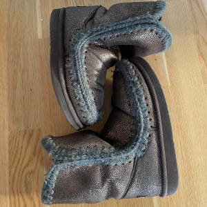 Mou skor  - Säljer ett par snygga bruna boots från Mou i  bra skick. De har en glittrig yta och är kantade med blå/grå stickade detaljer. Perfekta för höst och vinter, håller dig varm och stilren. Storlek 37 men passar mig som brukar ha 38