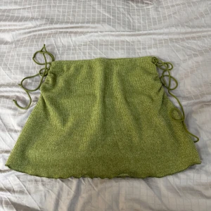 Grön stickad kjol - Säljer en superfin grön stickad kjol med knytband på sidorna. Perfekt för både vardag och fest! Kjolen har en bekväm passform och är i mycket bra skick. Den är idealisk för vår och sommar, och den gröna färgen ger en fräsch touch till din outfit.