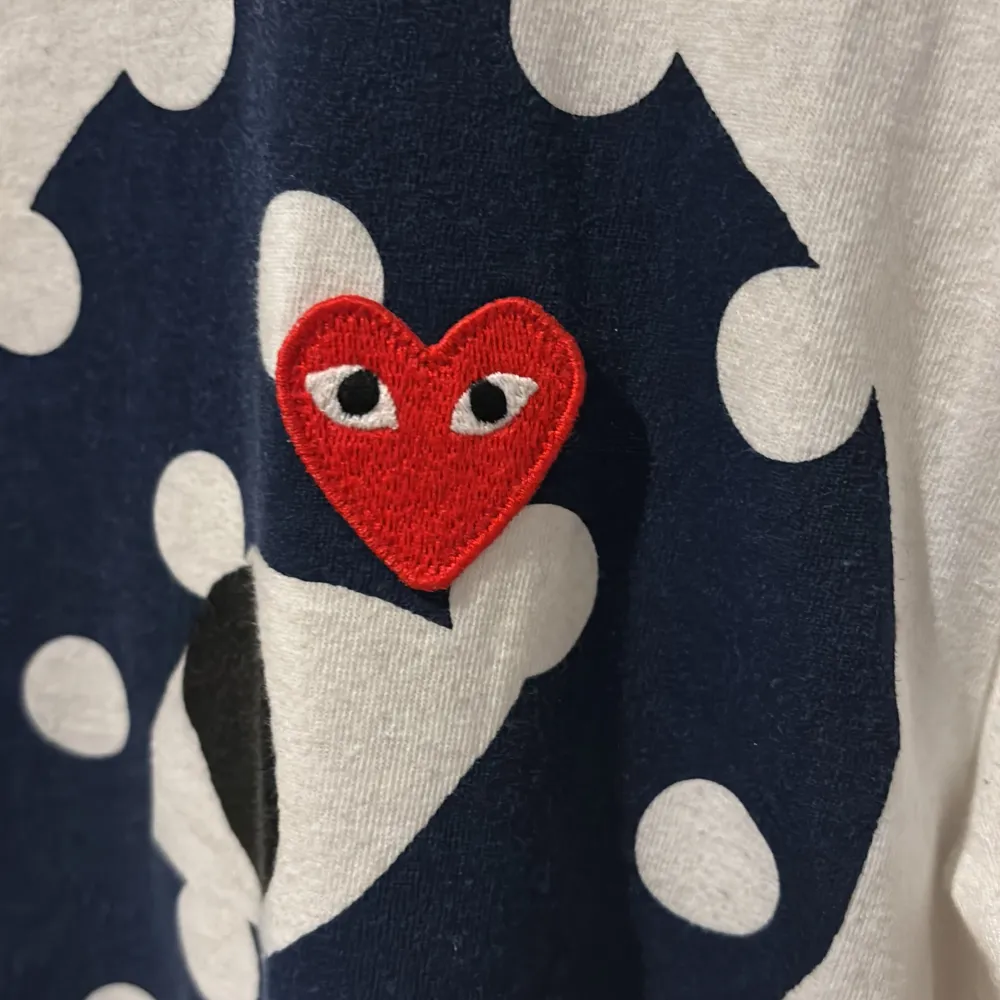 Säljer en vit t-shirt från Comme des Garçons med ett stort blått hjärta med vita prickar och ett rött broderat hjärta. T-shirten är kortärmad och i bra skick. Perfekt för en avslappnad stil!. T-shirts.