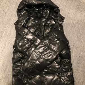 Svart puffet jacket - Säljer en snygg svart glansig puffet jacket som är NY!! Dragkedja och huva. Perfekt för kyliga dagar och ger en cool look. Jackan har en glansig finish och är i mycket bra skick. Passar både för höst och vinter.