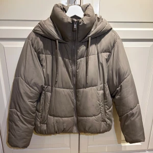 Beige pufferjacka från Zara - Säljer en snygg beige pufferjacka från Zara. Den har en dragkedja framtill och en mysig huva. Perfekt för kyliga dagar med sin quiltade design. Jackan är i mycket bra skick och passar perfekt till vintern! Säljer den nu för 250!