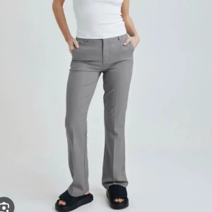 Grå kostymbyxor - Snygga grå kostymbyxor i normal passform. Perfekta för både kontoret och mer formella tillfällen. De har en klassisk design med dragkedja och knappar framtill. Byxorna är tillverkade i ett bekvämt material som ger en stilren look. Passar bra till både skjorta och t-shirt.