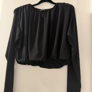 Svart långärmad topp från Gina Tricot - Snygg svart långärmad topp från Gina Tricot i ett mjukt och bekvämt material. Perfekt för både vardag och fest. Den har en lös passform med rynkade detaljer vid halsen som ger en elegant touch. Ett måste i garderoben för alla säsonger! Storlek L men passar även om man har strl M för den är lagom i storlek S,M,L beroende på hur man vill att den ska sitta 