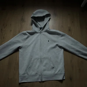 Grå hoodie från Polo Ralph Lauren - Säljer en stilren grå hoodie från Polo Ralph Lauren i storlek S då den tyvärr inte passar längre. Dragkedja framtill och en klassisk logga på bröstet. Inget slitage eller något sådant!
