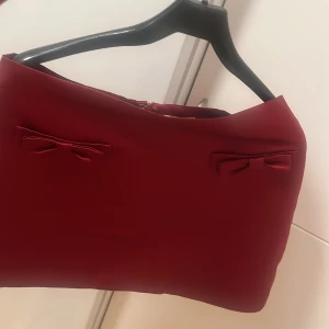 Röd kjol med rosetter - Säljer en elegant röd kjol med söta rosetter som detaljer. Perfekt för festliga tillfällen. Kjolen har en stilren design och är i mycket bra skick. Passar utmärkt för höst och vinter.