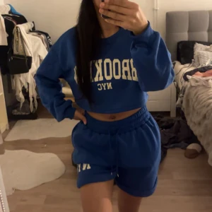 Blå croppad sweatshirt med text - Säljer en supercool blå croppad sweatshirt med texten 'BROOKLYN NYC' i vitt. Perfekt för en avslappnad stil eller en dag på stan. Den har långa ärmar och en bekväm passform. Matcha med shorts eller jeans för en komplett look!