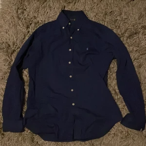 Mörkblå skjorta från Ralph Lauren - Säljer en snygg mörkblå skjorta från Ralph Lauren i bomull. Skjortan har långa ärmar och klassiska knappar framtill. Perfekt för både vardag och fest! 🕺