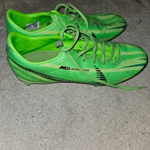 Gröna fotbollsskor från Nike - Säljer ett par grymma gröna Nike fotbollsskor i bra skick. De har en snygg design med svarta detaljer och snörning. Perfekta för fotbollsträning eller match. Sulan har bra grepp för gräsplaner. Skostorlek är herr 44. Passa på att uppgradera din fotbollsutrustning! ⚽️