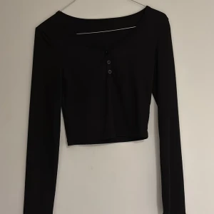 Svart långärmad croppad topp - Säljer en snygg svart långärmad topp med knappar framtill eftersom den aldrig används. Den är croppad och passar perfekt till både vardag och fest. Enkel men stilren design som funkar till det mesta. Perfekt för höst och vår! Fick den o present men den passade inte min stil. 