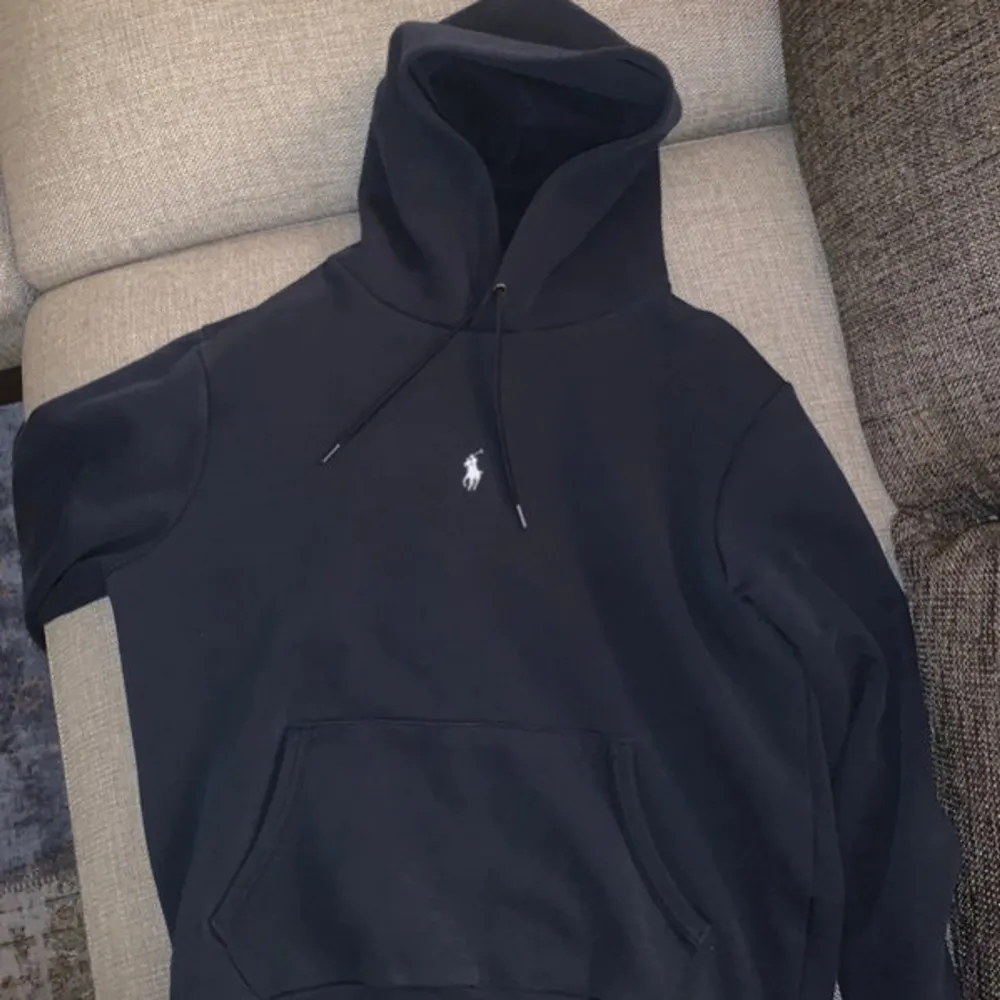 Säljer en klassisk marinblå hoodie från Polo Ralph Lauren. Den har en liten vit logga på bröstet och en stor ficka framtill. Perfekt för höst och vinter, och den är i mycket bra skick. Passar både till vardags och chillkvällar. 🖤. Tröjor & Koftor.