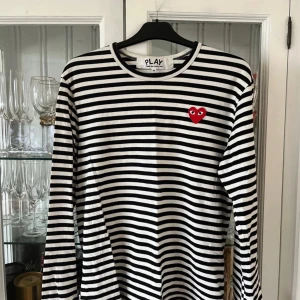 Randig tröja från Comme des Garçons - Säljer en superfin randig tröja från Comme des Garçons i svart och vit. Den har ett ikoniskt rött hjärta på bröstet. Perfekt för både vardag och fest! Tröjan är i mycket bra skick och har långa ärmar. Passar perfekt till jeans eller kjol.