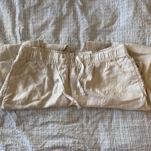 Beige linnebyxor från H&M - Säljer ett par bekväma beige linnebyxor från H&M i storlek M. De har en elastisk midja med snörning för extra komfort. Perfekta för en avslappnad stil under varma dagar. Byxorna är i bra skick och redo för nya äventyr!