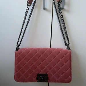 Rosa quiltad axelväska - Säljer en superfin rosa axelväska i quiltad stil. Väskan är gjord av sammet och har en snygg kedjerem i metall. Perfekt för att ge en touch av glamour till din outfit. Den är i nytt skick och har en praktisk storlek för alla dina nödvändigheter.       Aldrig använt🙏