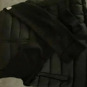 Svart cardigan från Moncler - Säljer en snygg svart dunjacka från Moncler. Den är i mycket bra skick och perfekt för medel kalla dagar. Cardiganen har en dragkedja framtill och en mysig huva. Den är stilren och passar till det mesta. Perfekt för både höst och vinter!