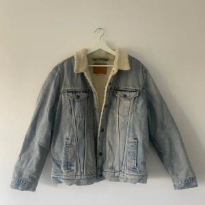 Jeansjacka med teddyfoder från Levi's - Säljer en snygg jeansjacka från Levi's i storlek L. Den har ett mysigt teddyfoder som gör den perfekt för höst och vår. Jackan är ljusblå med knappar framtill och två bröstfickor. Perfekt för en casual look! 🧥Lite smutsig på vissa ställen, se bilder. Men kan nog enkelt tvättas bort!