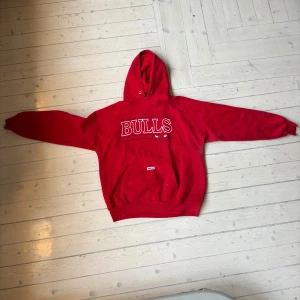 Röd Bulls hoodie från Ravens Athletic - Säljer en cool röd hoodie från Ravens Athletic med texten 'BULLS' på framsidan. Perfekt för en baggy fit med ett plagg som sticker ut. Den här små defekter såsom lite svarta prickar på framsidan men inget som förstör looken.