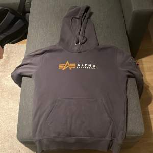 Säljer en snygg grå hoodie från Alpha Industries i storlek M. Den har en klassisk känguruficka och en cool detalj med en röd 'Remove Before Flight'-tag på ärmen. Perfekt för höst och vinter, och den är i mycket bra skick. Passar både till vardags och chillkvällar. Man ser inga tecken på användning. Tveka inte på att höra av er om ni har någon fråga!😊