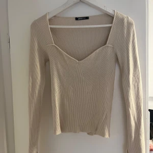 Beige ribbad topp från Gina Tricot - Säljer en superfin beige ribbad topp från Gina Tricot. Den har en v-ringad design och långa ärmar, perfekt för både vardag och fest. Toppen är i mycket bra skick och passar perfekt till höstgarderoben.
