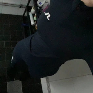 Mörkblå  långärmad topp  från J.Lindeberg - Säljer en mörkblå långärmad tröja från J.Lindeberg. Den har en halv dragkedja framtill och en vit logga på bröstet. Perfekt som vanlig tröningströja och underställ. Tröjan är i mycket bra skick och passar både till vardags och träning. Finns ej i ordinarie sortiment då det är sampel men nypris är ca 1400