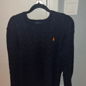 Mörkblå stickad tröja från Polo Ralph Lauren - Säljer en snygg mörkblå stickad tröja från Polo Ralph Lauren. Den har ett klassiskt flätmönster och den ikoniska loggan broderad i orange på bröstet. Perfekt för höst och vinter, med långa ärmar och en bekväm passform. Passar både till vardags och lite finare tillfällen. Ny pris på denna ligger på ca 2500kr, mitt pris 450kr!! Hör av er för fler bilder eller funderingar 😁