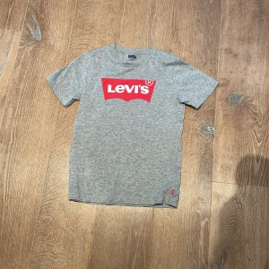 Grå t-shirt från Levi's - Säljer en snygg grå t-shirt från Levi's i storlek 12A (152 cm). Den har en klassisk röd och vit Levi's-logga på bröstet. Perfekt för vardagsbruk och passar till det mesta. T-shirten är i bra skick och gjord av mjuk bomull. Perfekt för både vår och sommar! Pris kan diskuteras!