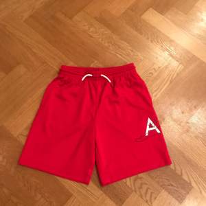 Säljer ett par röda Jordan shorts i mycket bra skick för barn. Storlek: M/10-12år 132-147cm. De har en elastisk midja med vit snörning och ett stort 'AIR' tryck med den ikoniska Jordan siluetten på sidan. Perfekta för basket men funkar också super till andra sporter. Superbekväma och stilrena!