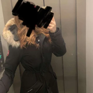 Svart parkajacka med päls från Canada Goose - Säljer en snygg och varm svart parkajacka från Canada Goose. Jackan har en fluffig pälsfodrad huva och stängs med både dragkedja och knappar.Inga skador alls.  Perfekt för kalla vinterdagar! 🖤
