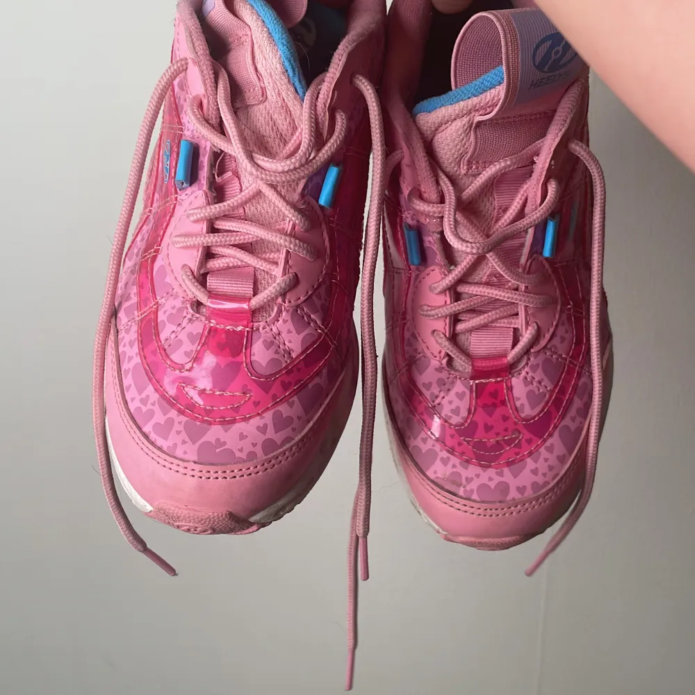 Säljer ett par rosa Heelys i funktionsdugligt skick (Fläckar odyl efter andvändning finns) med hjärtan på sidorna. De har snörning och en cool hjuldesign under sulan för att rulla runt. Perfekta för att glida fram med stil! 💖. Skor.